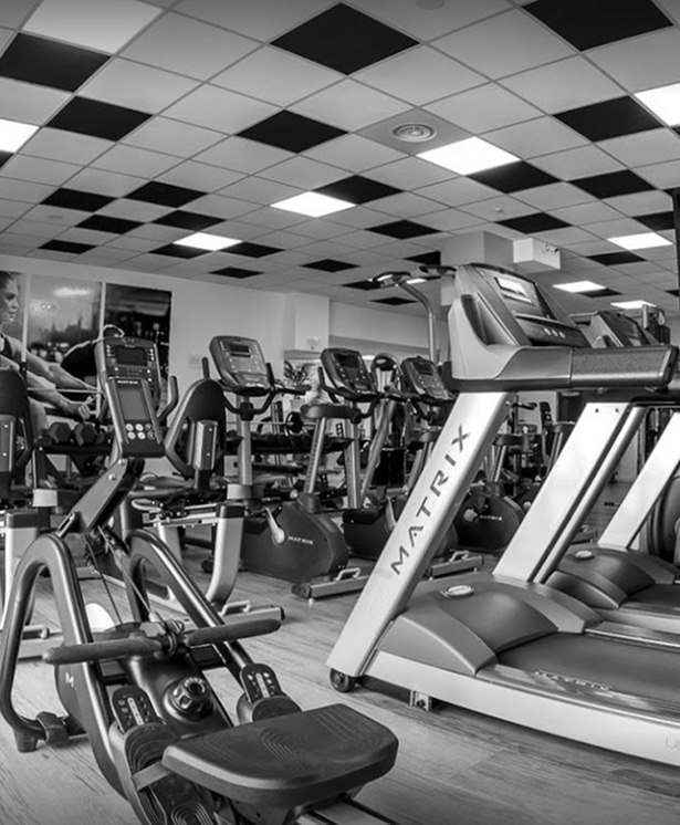 Intérieur de salle de sport moderne en noir et blanc, vue rapprochée sur un rameur Matrix et des tapis de course Matrix, avec un plafond à damier lumineux.